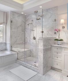 a white bathroom with marble flooring and walls, along with a walk in shower