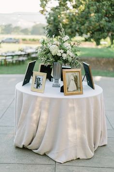 a table topped with pictures and flowers on top of a white cloth covered round table