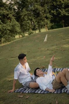 a man and woman laying on a blanket in the grass with a kite flying above them