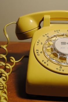 an old fashioned yellow telephone sitting on top of a wooden table next to a phone cord