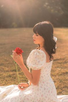 a woman in a white dress is holding a red rose while sitting on a blanket