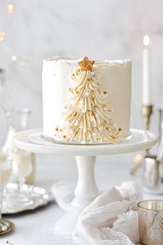 a white frosted cake with a gold christmas tree decoration on the top is sitting on a plate