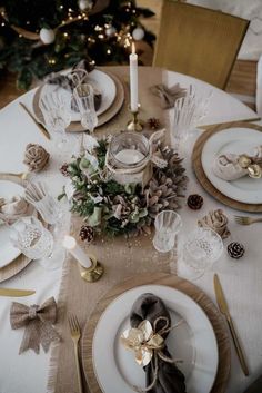 a table set for christmas dinner with pine cones, silverware and candlesticks