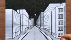 a hand holding up a drawing of a city street at night with buildings and stars in the sky