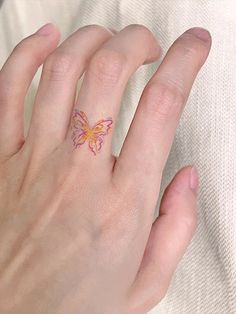 a woman's hand with a butterfly tattoo on her left thumb and pink ink