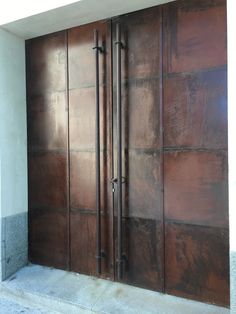 two brown doors are open on the side of a building in front of a concrete wall