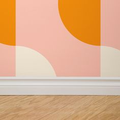 an orange vase sitting on top of a wooden floor next to a pink and yellow wall