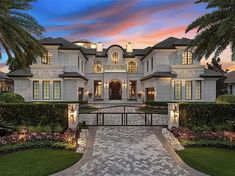 a large white house with palm trees in the front yard and landscaping around it at dusk