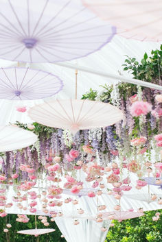 several umbrellas hanging from the ceiling with flowers on them and greenery in the background