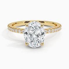 a yellow gold engagement ring with an oval cut diamond in the center and pave set shoulders