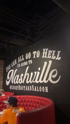 a man sitting on top of a red couch in front of a sign that says, you can all go to hell