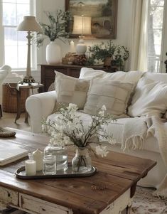 a living room filled with white furniture and flowers on top of a wooden coffee table