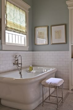 a white bath tub sitting in a bathroom next to a sink and window with pictures on the wall