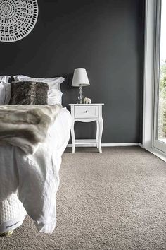 a bedroom with gray walls and carpeted flooring has a white bed in the corner