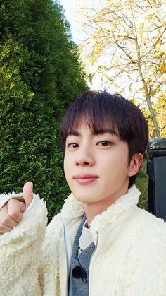 a young man in a white jacket and tie pointing at the camera with trees behind him