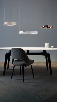 a dining table with chairs and lights hanging from it's ceiling, in front of a gray wall