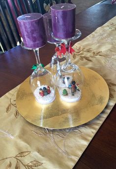 two wine glasses sitting on top of a gold plate with purple candles in the middle