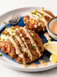 two crab cakes on a plate with sauce and lemon wedges