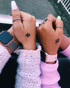 two people with matching wrist tattoos holding their hands up to the camera and pointing fingers at each other