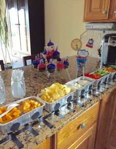 a kitchen counter topped with trays of fruit and veggies