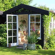 a garden shed with potted plants in the front and windows on the back side