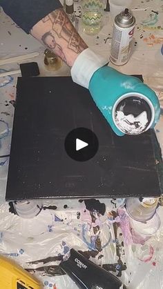 a person is painting on a table with paint and other items around it, including a laptop