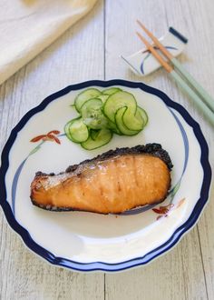 a plate with some fish and cucumbers on it next to chopsticks