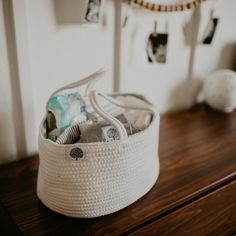 a white basket sitting on top of a wooden table next to a wall hanging with pictures