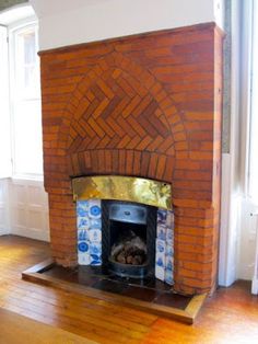 an old brick fireplace in the corner of a room with wood floors and windows on both sides