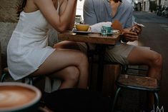 two people sitting at a table eating food and talking on their cell phones while drinking coffee