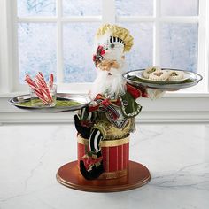 a santa clause holding two trays of food on a table next to a window