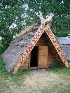 an old thatched hut with a decorative design on the door and side walls, in a grassy area next to some trees