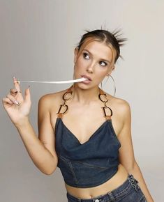 a woman holding a knife in her mouth and looking at the camera while wearing jeans