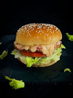 a cheeseburger with lettuce and tomato on a black surface, ready to be eaten