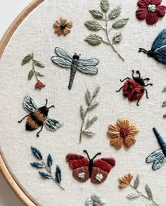 a close up of a embroidery on a hoop with bugs and flowers in it,