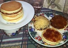 three pancakes on plates with grated cheese and syrup are sitting on a plaid tablecloth