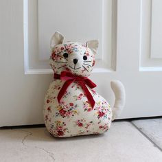 a stuffed cat sitting in front of a white door with a red bow on it's neck