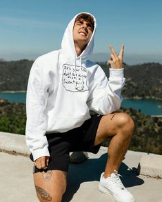 a man sitting on top of a cement slab wearing a white hoodie and black shorts