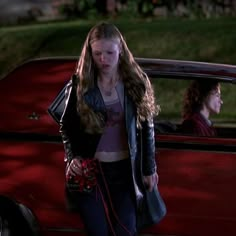 a woman standing next to a red car on the street in front of another woman