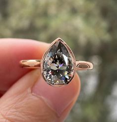 a person holding a ring with a pear shaped diamond in it