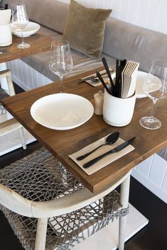 a wooden table topped with white plates and silverware next to a gray couch covered in pillows