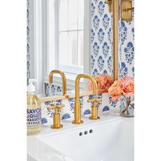 a bathroom sink with gold faucets and blue wallpaper