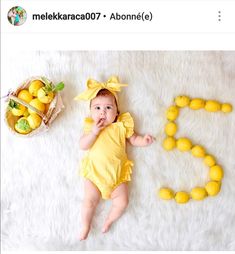 a baby in a yellow outfit laying next to some lemons on a white blanket