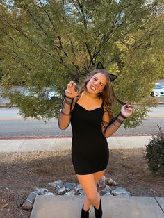 a woman in a black dress is posing for the camera with her hands up and smiling