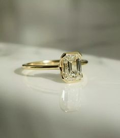 a yellow gold ring with an emerald cut diamond in the center on a white surface