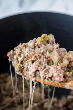 a wooden spoon full of food being held up by someone's hand in a skillet