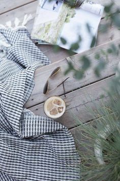 a cup of coffee sitting on top of a wooden table next to a plaid blanket