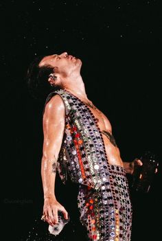 a man with his eyes closed wearing a sequined vest and holding a bottle