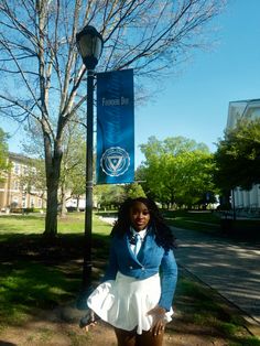 a woman standing in front of a lamppost with a sign on it's pole