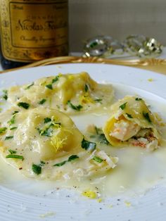 a white plate topped with ravioli covered in cheese and sauce next to a bottle of wine